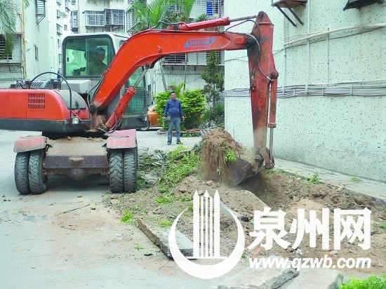 挖掘机正在将小区里的绿化带连根挖起