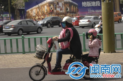 骑电动车的女士将孩子的书包背在身前