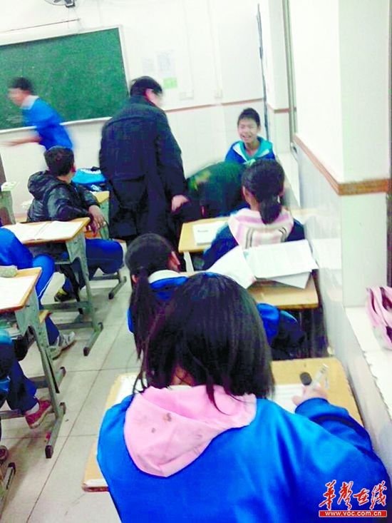 一名老师模样的男子右手正摁在一名男生后颈处