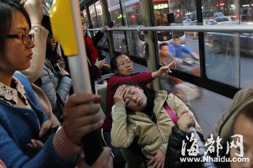 晕倒的女子手摸额头坐在座位上，后面的女乘客帮忙打 