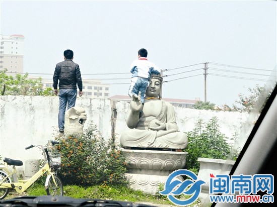 一小孩子和父亲为了看墙外小狗，将雕塑当垫脚石