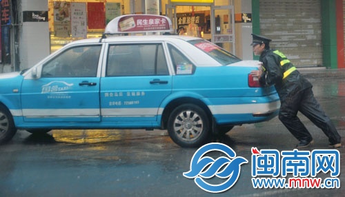 一名协警奋力推车，帮助的哥将车辆移走