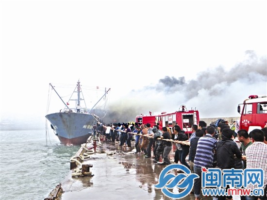 一群人帮忙拉缆绳，将失火渔船固定