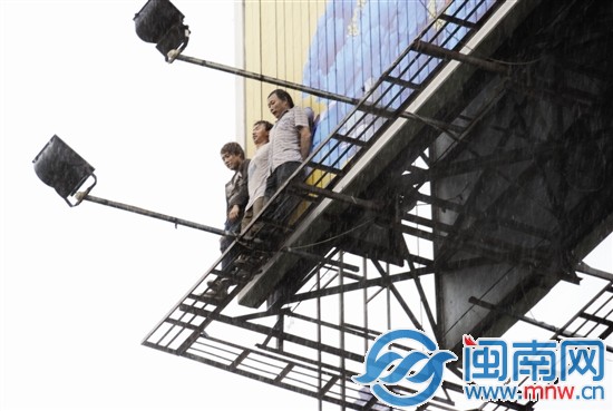 大雨中，几名工人紧贴广告牌，但浑身已被淋湿